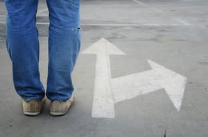 Person standing on road next to sign going two directions