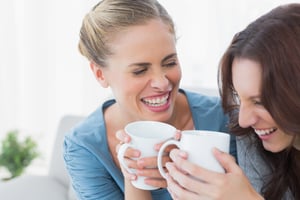 Friends bursting out laughing while having coffee sitting on the sofa