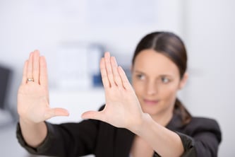 Mid adult businesswoman making hand frame in office, focus hands