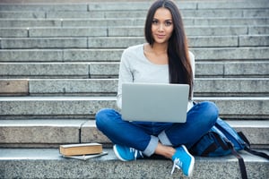 Portrait of a happy young woman sitting on the city stairs and using laptop computer outdoors