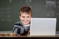 Portrait of male student smiling with laptop on desk in classroom