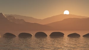 Stones across a pond at sunset with mountain in background