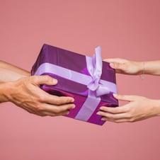 close-up-two-hands-holding-purple-gift-boxes-against-colored-background