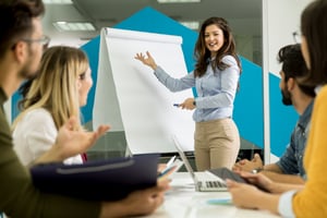 confident-young-team-leader-giving-presentation-group-young-colleagues-as-they-sit-grouped-by-flip-chart-office