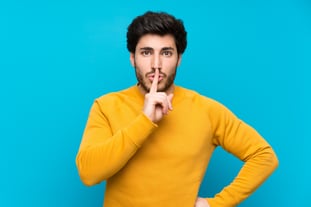 handsome-isolated-blue-wall-showing-sign-silence-gesture-putting-finger-mouth