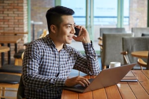 side-view-asian-guy-having-phone-call-while-working-laptop