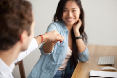 smiling-asian-young-woman-fist-bumping-male-colleague-work