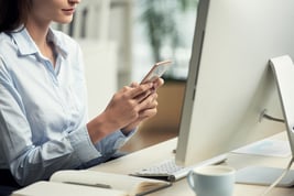 unrecognizable-woman-sitting-office-front-computer-using-smartphone