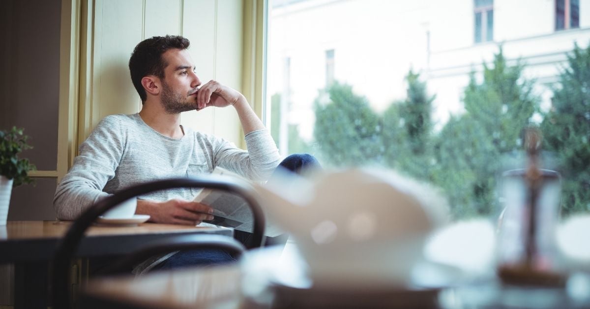 Man staring thoughtfully out the window with a book or notebook in his hands