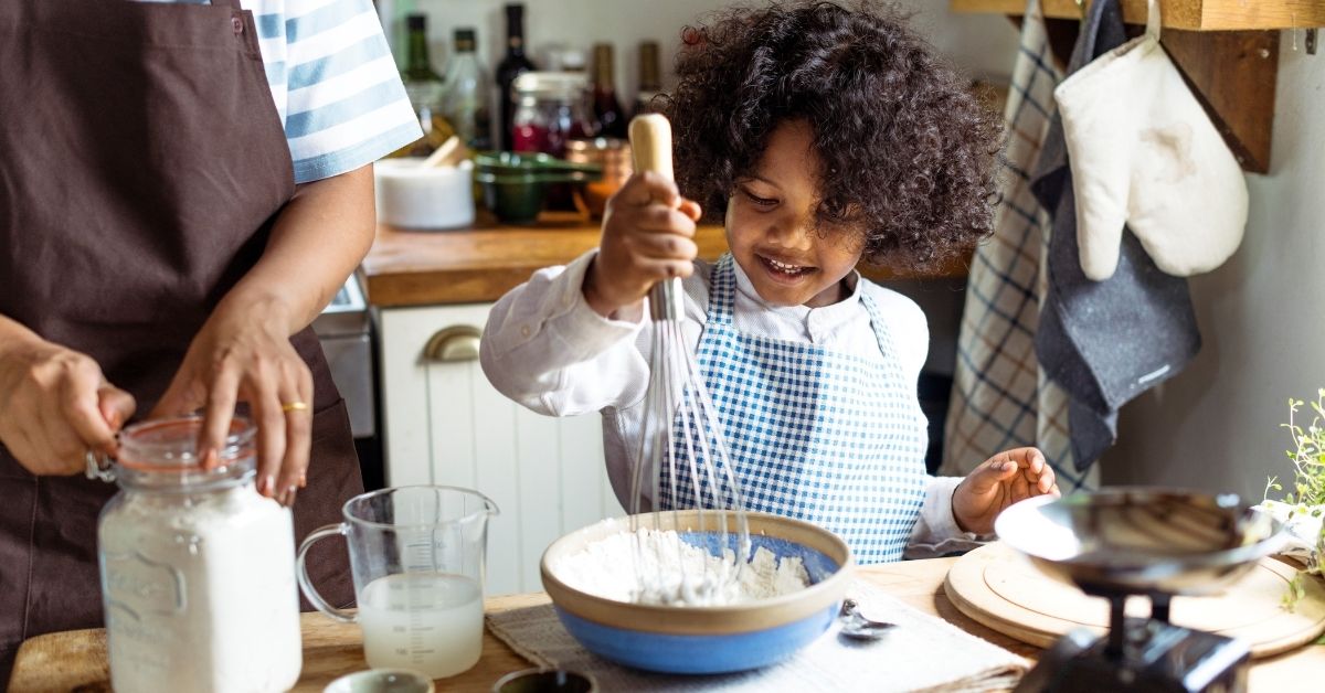 small child whisks something in a bowl while baking with adult