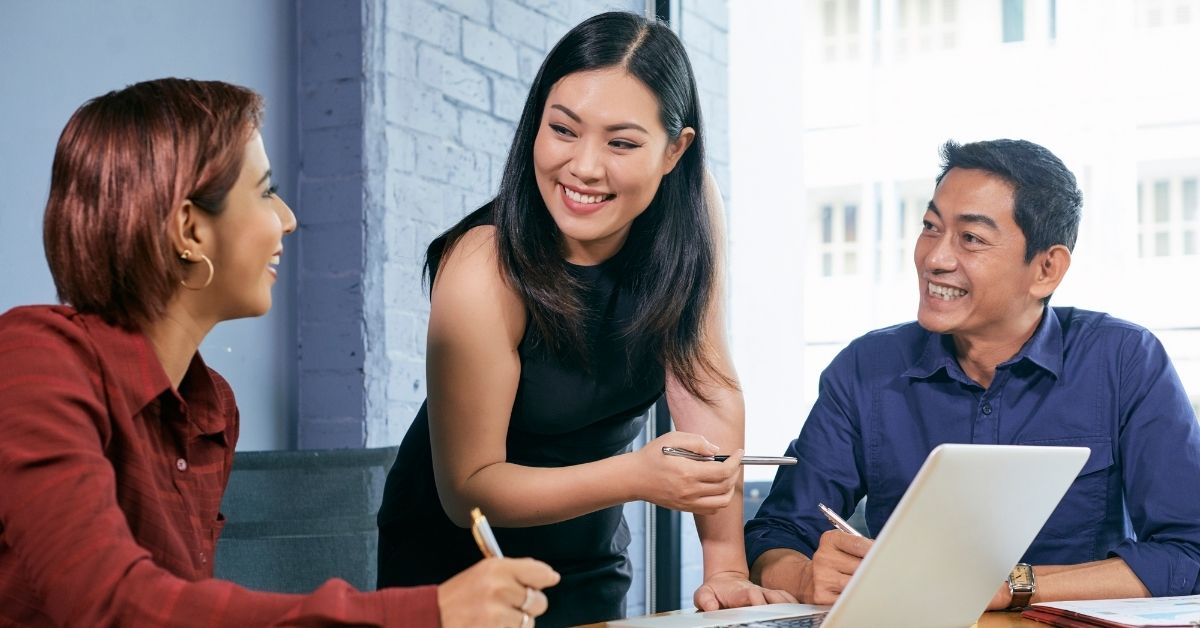 Diverse trio-manager, worker, and intern-looking at each other smiling in front of a laptop.