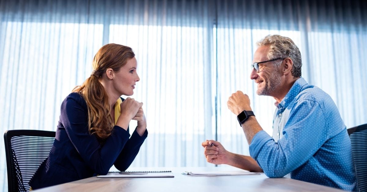 employee and boss talking leaning in over a conference table