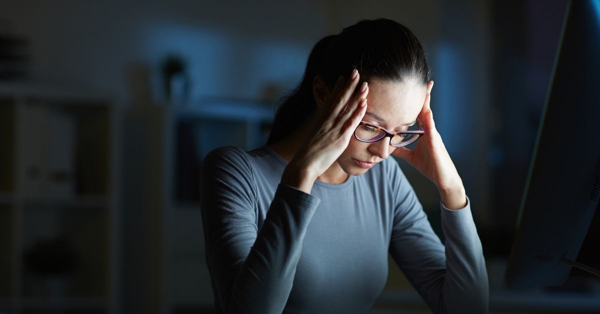 Stressed woman looking down with her hands on her temples in a dark room