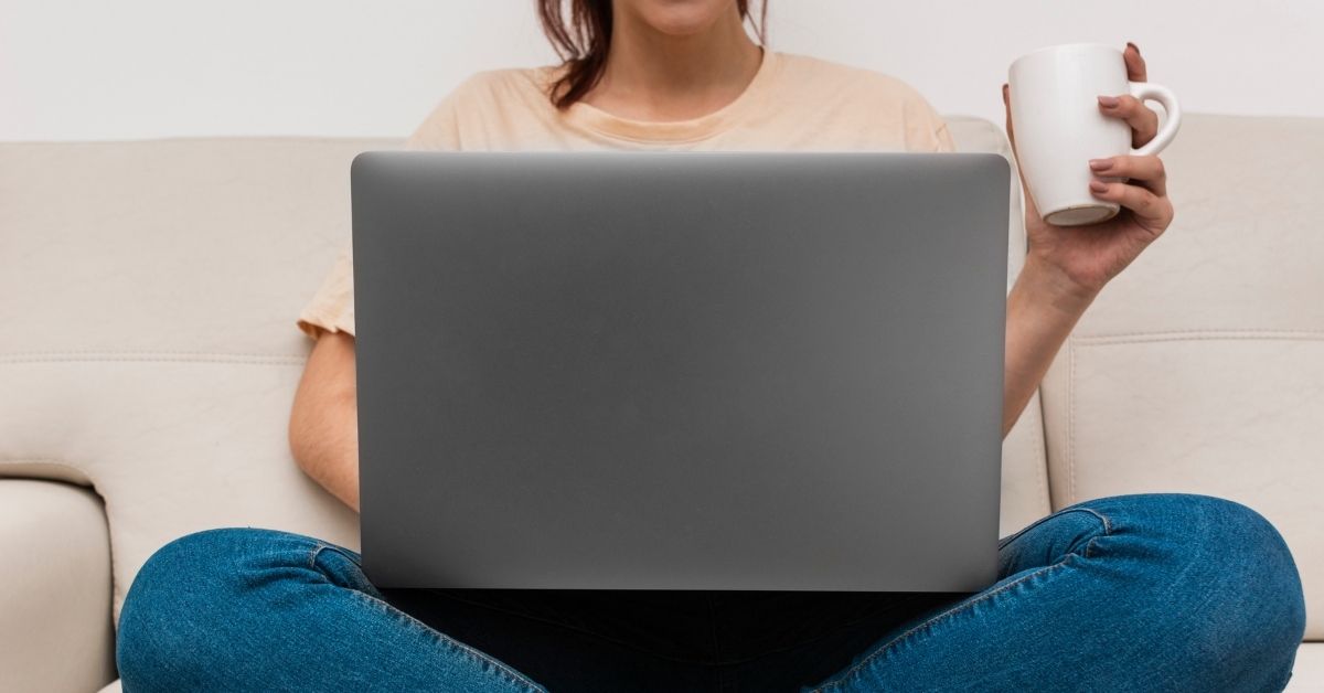 woman sitting cross-legged with a laptop on her lap and a mug in her hand