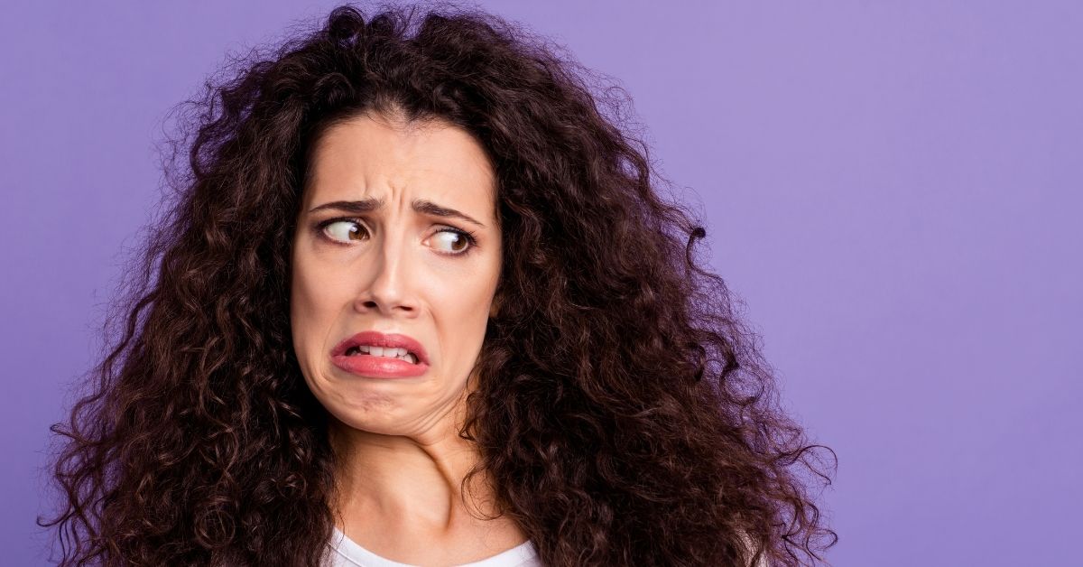 woman on purple background with big curly hair giving 'ugh' face of disgust looking to the side 