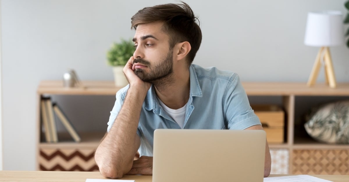 Man at computer staring off into space, distracted and unproductive