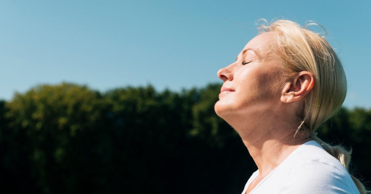 woman standing in the sunlight with her eyes closed taking in the vitamin d breathing and being mindful