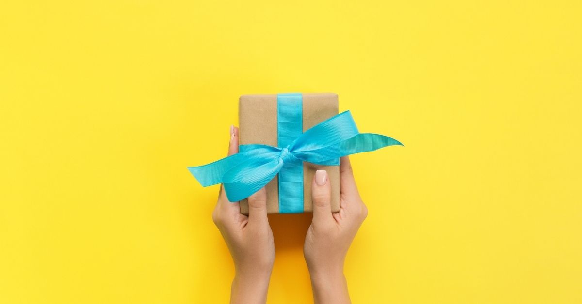 hands holding a gift wrapped in brown paper and a blue bow on a yellow background