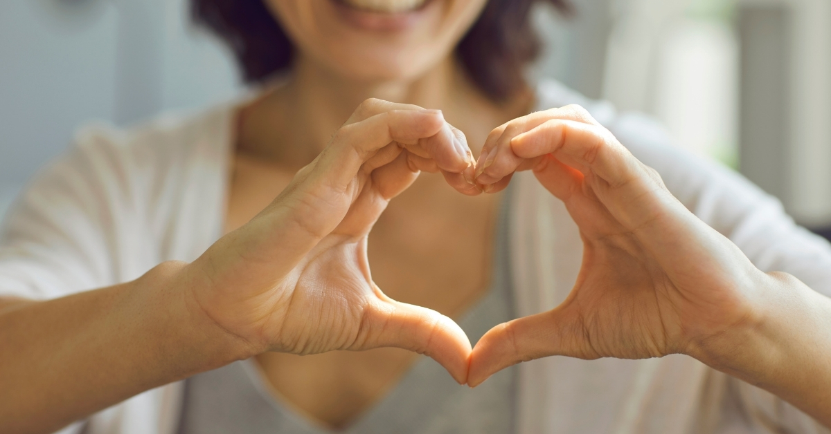 person standing with their hands out making a heart shape, smiling