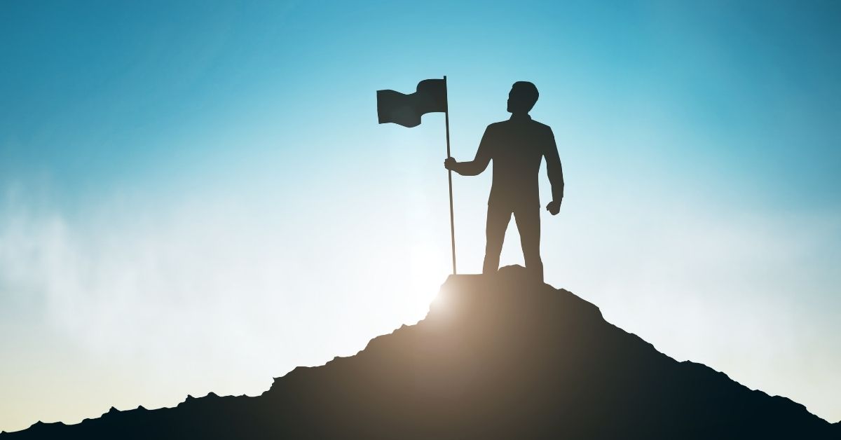 person standing on top of hill with flag in sunlight