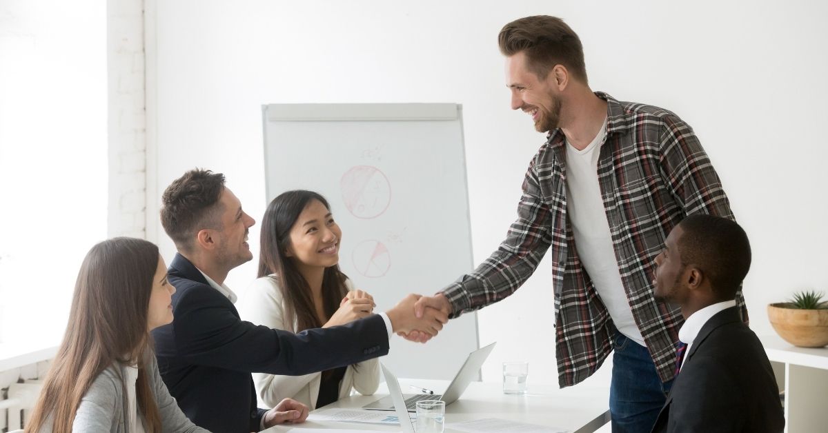 smiling-businessman-welcoming-new-partner-group-meeting-with-handshake