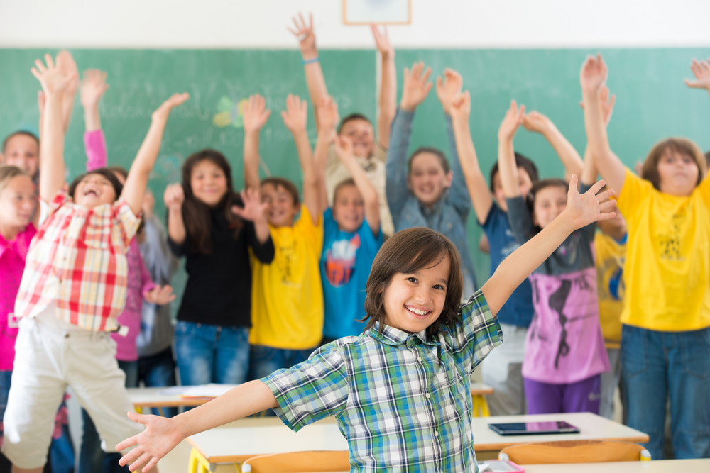 Group of kids having up rising hands with books in classroom