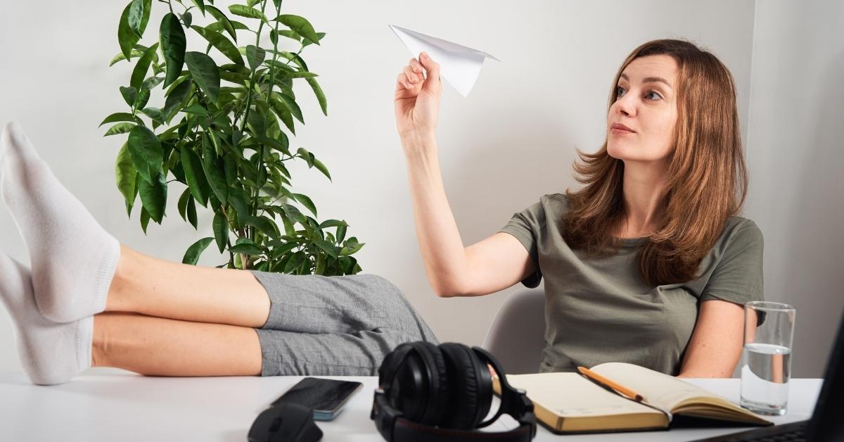 woman with feet up on her desk flying a paper airplane